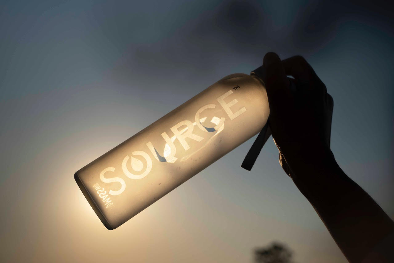 A bottle of SOURCE Global drinking water held up to the light.